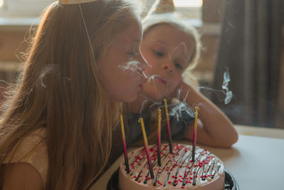 Little twin girls, children blow out candles cake birthday party at home. holiday during quarantine