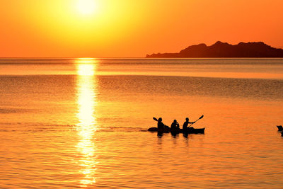 Silhouette people on sea against orange sky