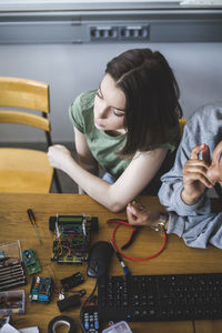 High angle view of female teenage students sitting with robot at desk in classroom