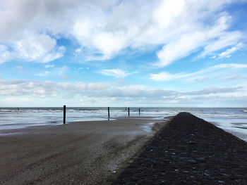 Scenic view of calm beach against cloudy sky