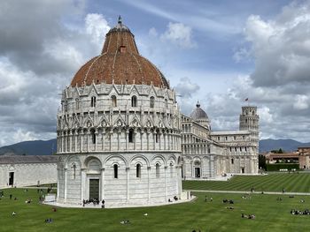 View of historic pisa baptistery against cloudy sky and the leaning tower of pisa at back 