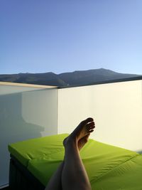 Low section of man relaxing on mountain against clear sky