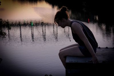 Woman sitting on pier by lake at dusk