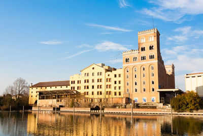 Buildings by river against sky in city