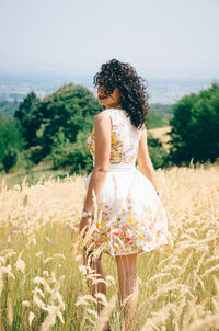 Young woman standing amidst plants on field against clear sky during sunny day