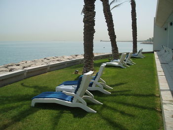 Deck chairs on grass by sea against clear sky