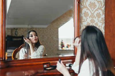 Young woman doing make-up while looking at mirror