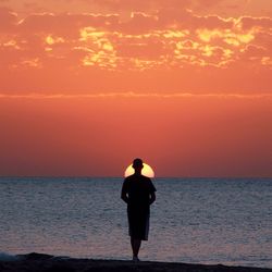 Silhouette man standing on beach against sky during sunset