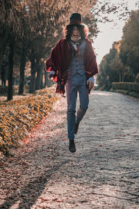 Full length portrait of laughing man cosplaying mad hatter jumping on footpath