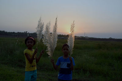 Siblings standing on field against sky