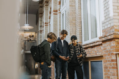 Teenage boy sharing mobile phone with friends while walking in school corridor