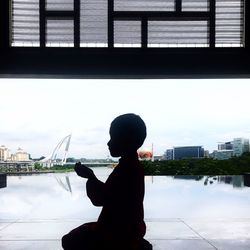 Side view of silhouette woman standing by river in city