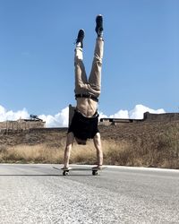 Full length of man doing handstand on road against sky