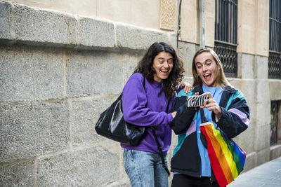 Two friends taking a selfie while walking in the street outdoors with lgbt flag.