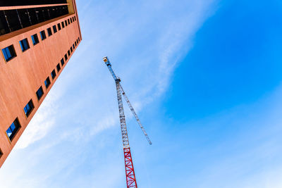 Low angle view of crane by building against sky