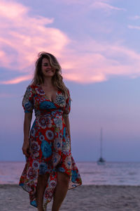 Young woman standing at beach against sky during sunset