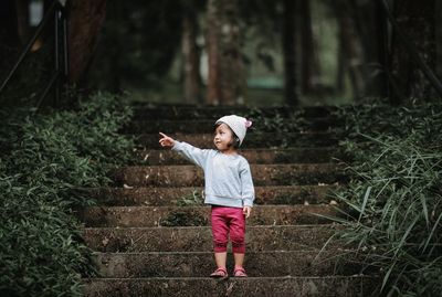 Full length of girl gesturing while standing on steps in forest