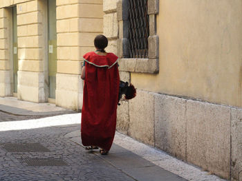 Rear view of man walking on footpath against building