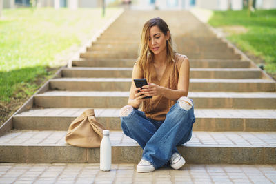 Young woman using mobile phone while sitting on staircase