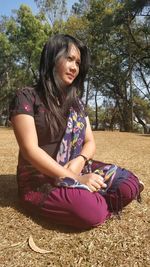 Young woman sitting on field against trees