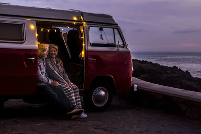 Senior couple traveling in a vintage van, watching sunset at the sea