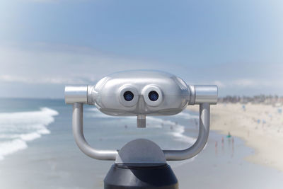 Close-up of coin-operated binoculars over beach against sky