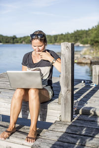 Mid adult woman using laptop on pier