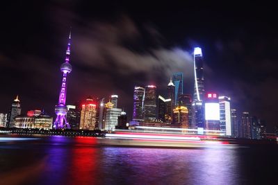 Illuminated oriental pearl tower by huangpu river against sky in city at night