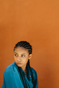 Young woman looking away by orange wall