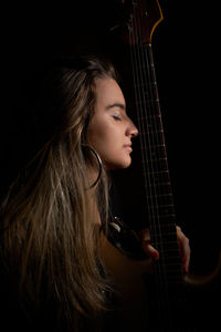 Young woman playing guitar against black background