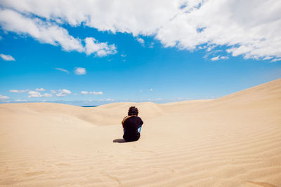 Man sitting on sand dune in desert against sky