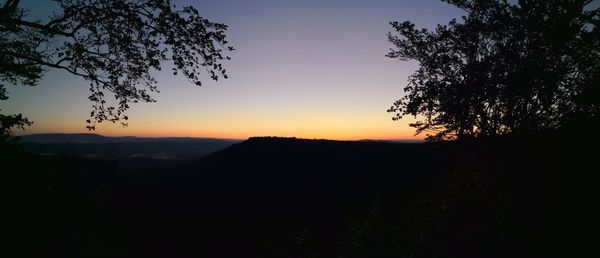 Silhouette trees on landscape against sky at sunset