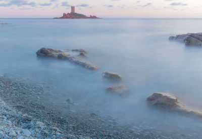 Scenic view of sea and island against sunset sky