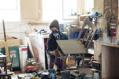 Female carpenter examining wooden chair in workshop