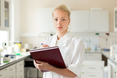 Portrait of woman holding book standing at laboratory