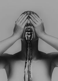 Naked woman with dripping face paint covering eyes against gray background