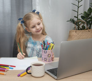 Girl drawing over paper by laptop on table