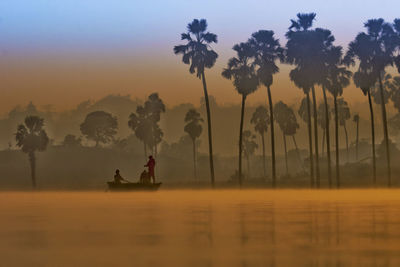 Silhouette people sitting by lake against sky during sunset
