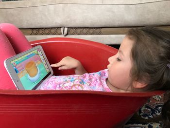Close-up of cute girl using digital tablet while lying in container