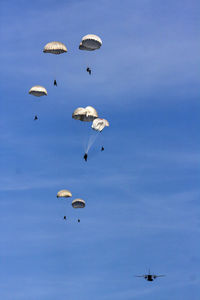 Low angle view of people paragliding against sky