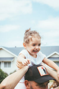 Father holding daughter on shoulder against sky