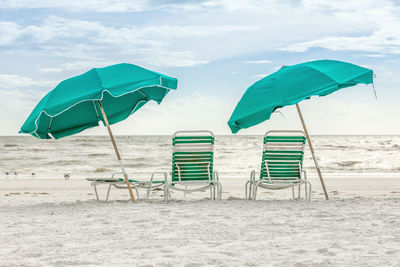 Deck chairs with parasols at beach against sky