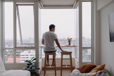 Rear view of man standing by window at home