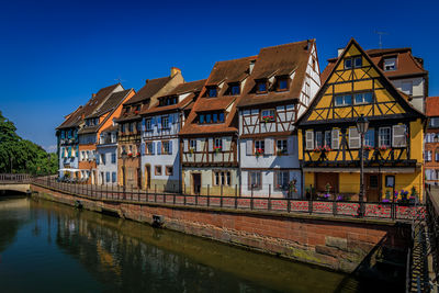 Buildings by river against clear blue sky