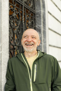 Joyful senior man in green jacket gazing upwards near ornate metal gate, lifestyle concept