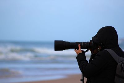 Side view of photographer with dslr at beach against sky