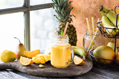 A tropical mango citrus smoothie on a rustic board surrounded by fruit.