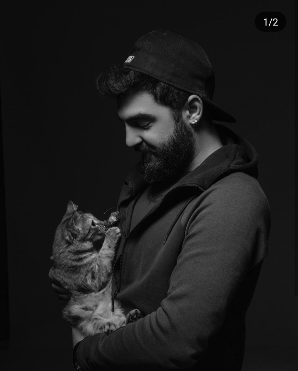 black, cat, one person, black and white, monochrome photography, adult, darkness, monochrome, young adult, beard, white, portrait, facial hair, clothing, indoors, men, black background, waist up, animal, studio shot, hat, person, carnivore, animal themes, one animal, looking, side view, pet, fashion, domestic animals, dark, mammal, cap, casual clothing, fashion accessory, human face, hipster, lifestyles, holding