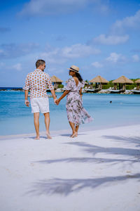 Rear view of couple holding hands while standing on beach