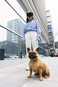 Happy businesswoman wearing virtual reality simulator standing with dog on footpath